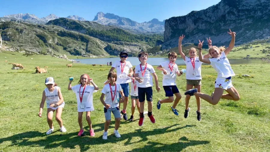 Gruppe von Teilnehmern des The Village Sommerlagers springen vor einem See in den asturischen Bergen