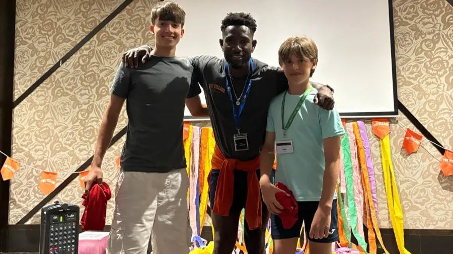 Dos jóvenes participantes en el campamento internacional the Village posan con su coach al recibir un premio