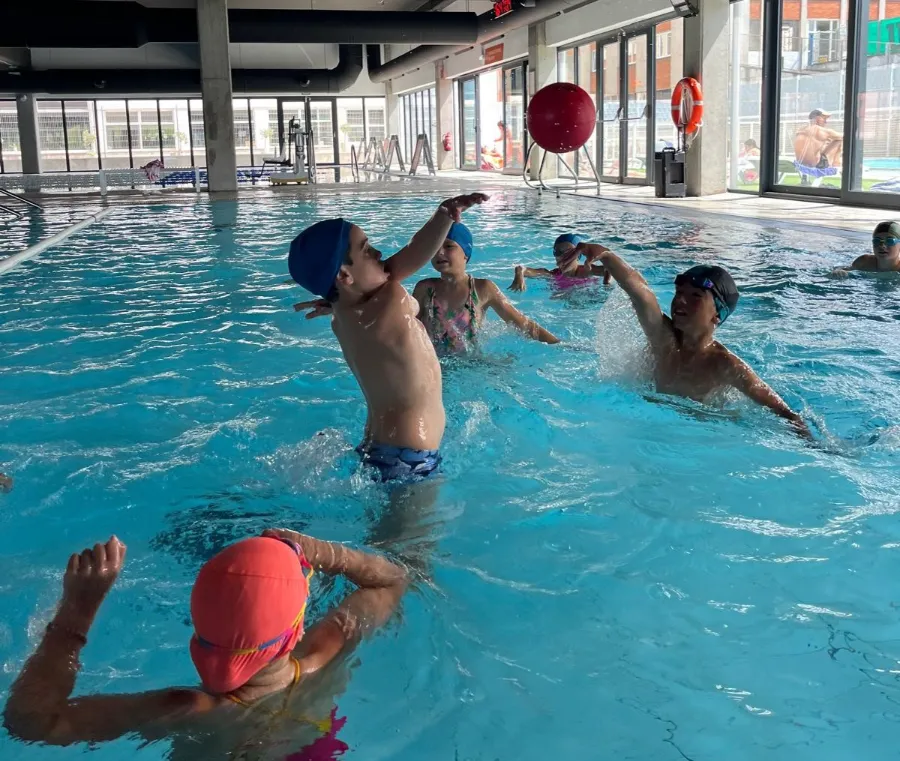 Grupo de niños jugando a la pelota en la piscina climatizada del campamento en inglés