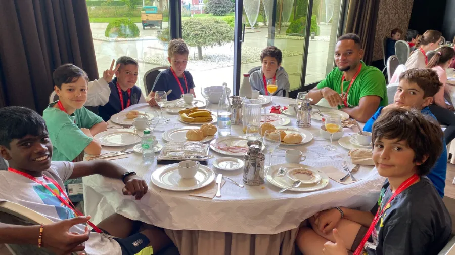Grupo de adolescentes conversan con su coach internacional en el desayuno del campamento en inglés