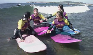 Englischcamp. Surflehrer, der einer Gruppe von 5 Kindern am Strand von Salinas eine Lektion über Wellen, Wind und Strömungen gibt.