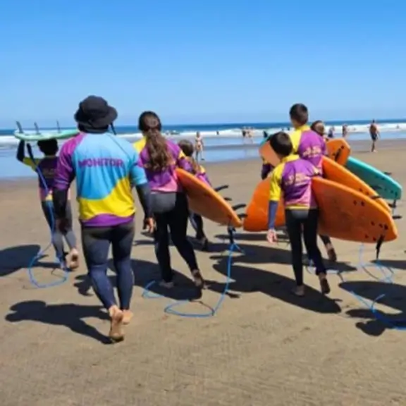 Gruppe von Kindern mit Surfbrettern auf dem Weg zum Meer im Sommerlager in Spanien