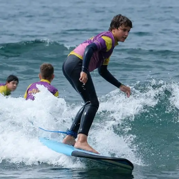 Kind surft auf einer Welle am Strand von Salinas im Sommerlager in Spanien