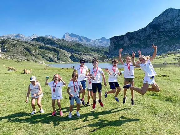 Kinder springen an einem See während eines Ausflugs in Asturien mit ihrem internationalen Coach an einem sonnigen Sommertag in einem Sommercamp in Spanien.