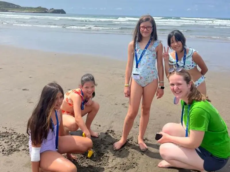 Vier Mädchen unterhalten sich mit ihrem internationalen Coach am Strand während des Sommercamps für Kinder in Spanien