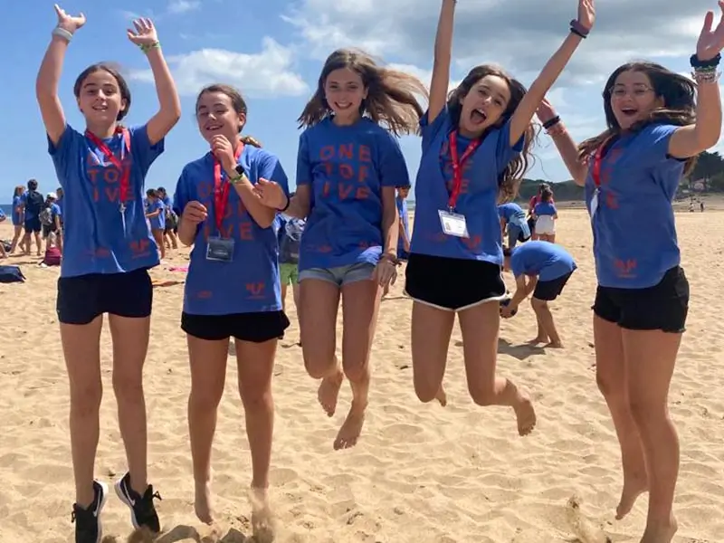 Eine Gruppe von Mädchen, die am Strand in Asturien während des Sommercamps für Kinder in Spanien Spaß haben und springen