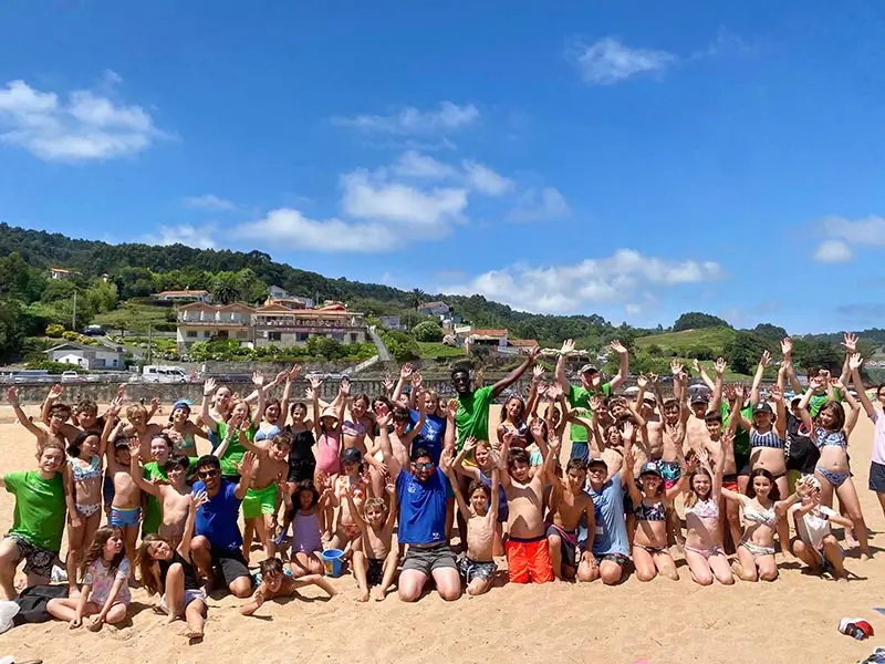 Kinder und internationale Coaches spielen an einem sonnigen Strand in Asturien während des Sommercamps für Kinder in Spanien