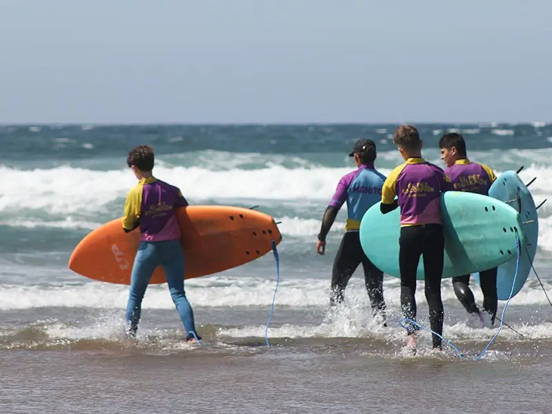 Gruppe von Jugendlichen aus dem Englisch Sommercamp in Spanien, die am Strand zur Surfstunde gehen