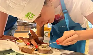 A group of children in a summer camp, learning cooking techniques and practicing English with experienced chefs.