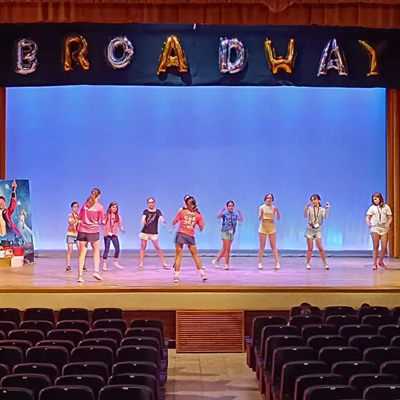 Participants rehearsing a dance on the stage at the summer camp