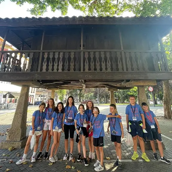 Participants under a traditional Asturian hórreo during a summer camp excursion