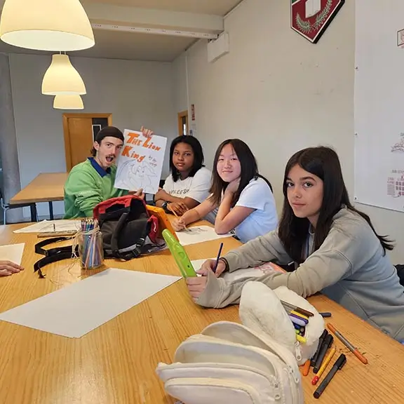 Three participants preparing scripts with their coach during the Media activity at the summer camp