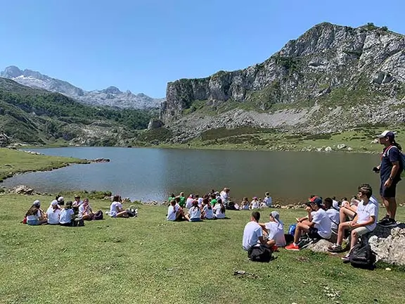 Group of young people jumping by a lake with their international coach on a sunny excursion day at a summer camp in Spain.