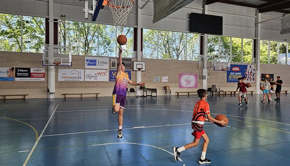 Young participants playing basketball in the indoor sports hall at the summer camp in Spain