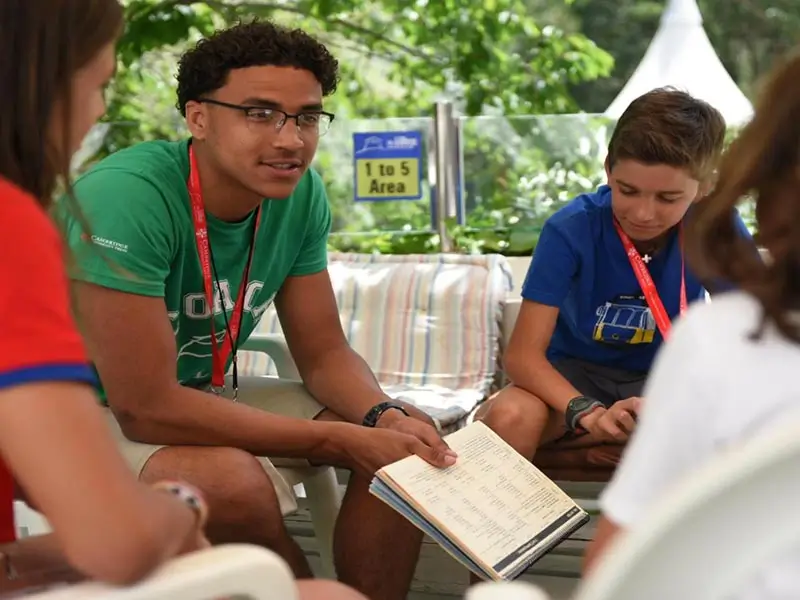 An international coach talking with five children using the Cambridge workbook