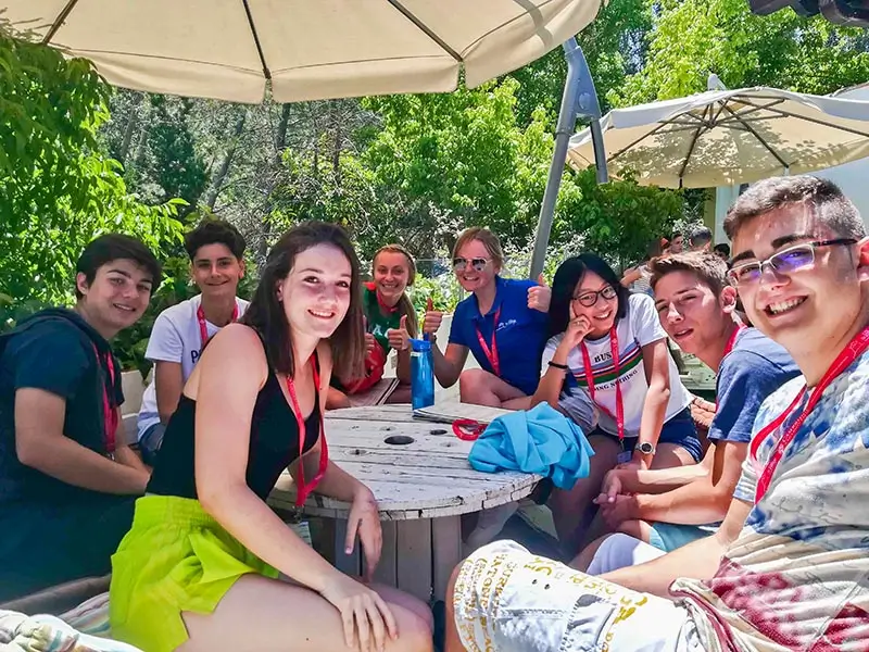 Participantes conversando con sus coaches internacionales en un día soleado de verano en el campamento inglés en España the Village