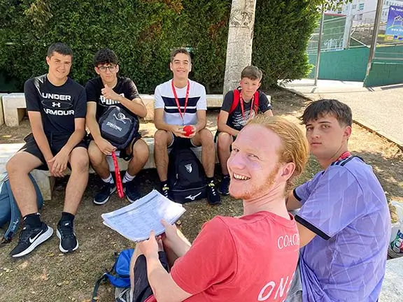 Un coach avec cinq jeunes discutent en plein air au camp d’anglais, suivant la méthode supervisée par Cambridge University Press